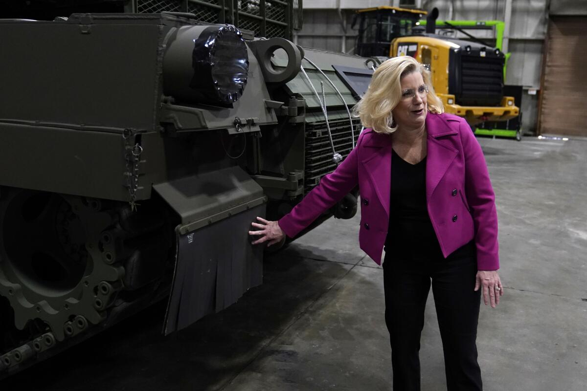 Christine Wormuth touches the front of an M1A2 Abrams main battle tank in a warehouse.