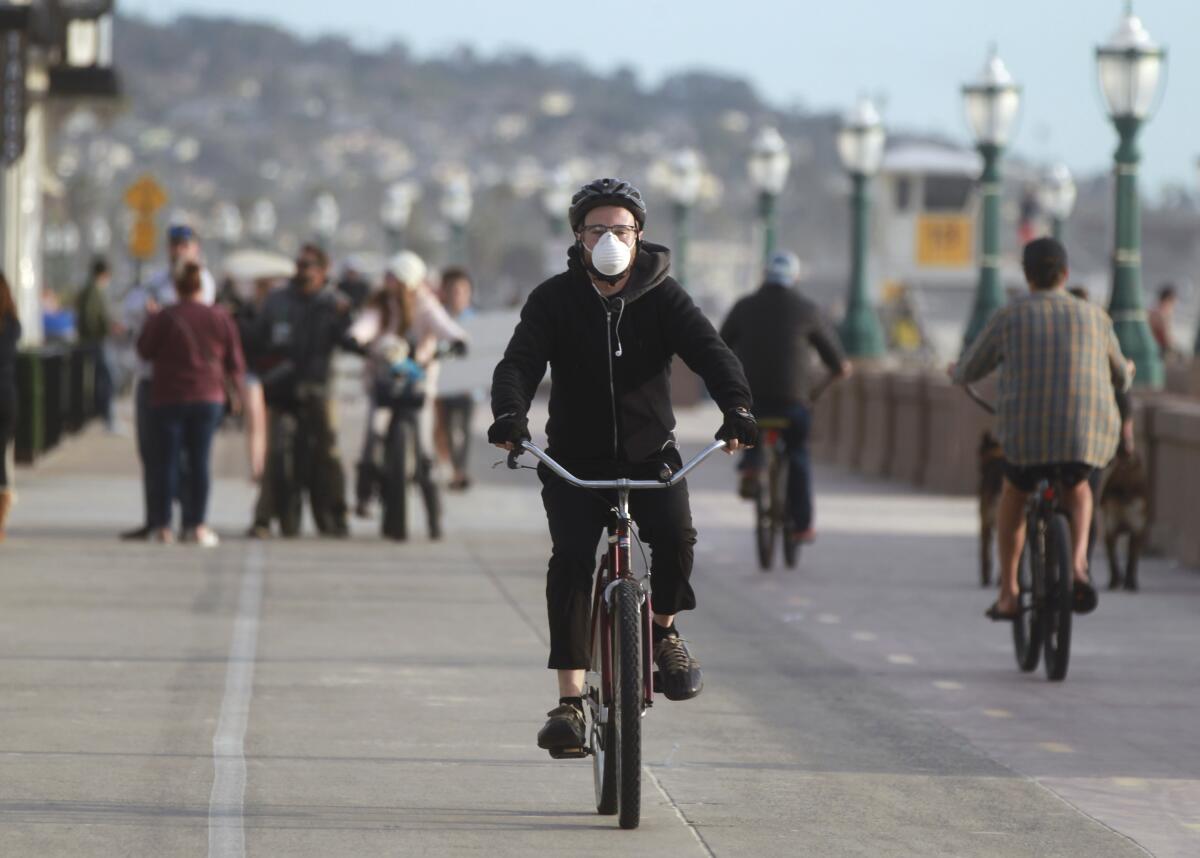 A Mission Hills resident wears a mask as he rides his bike on Mission Beach Boardwalk.
