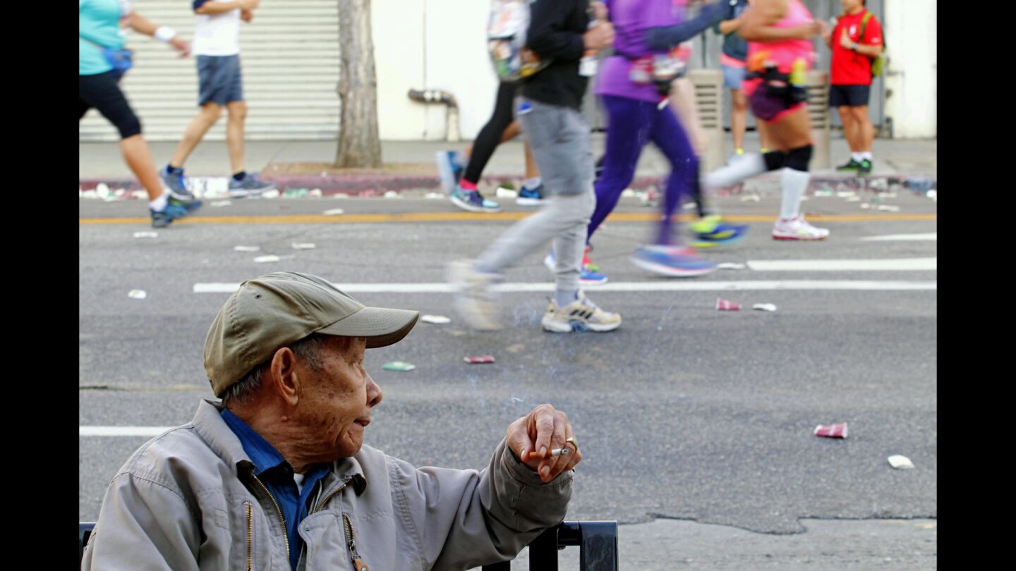 A man watches runners pass by during the 30th Los Angeles Marathon in Chinatown.