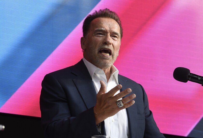 Arnold Schwarzenegger, in jacket and open-collar shirt, gestures while speaking into a microphone.
