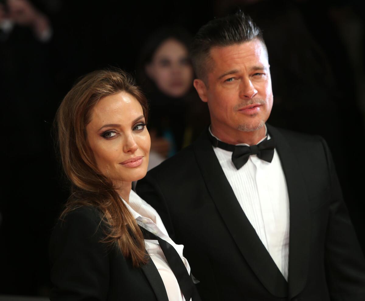Actors Angelina Jolie and Brad Pitt pose at an event wearing black tuxedos, with her bowtie undone