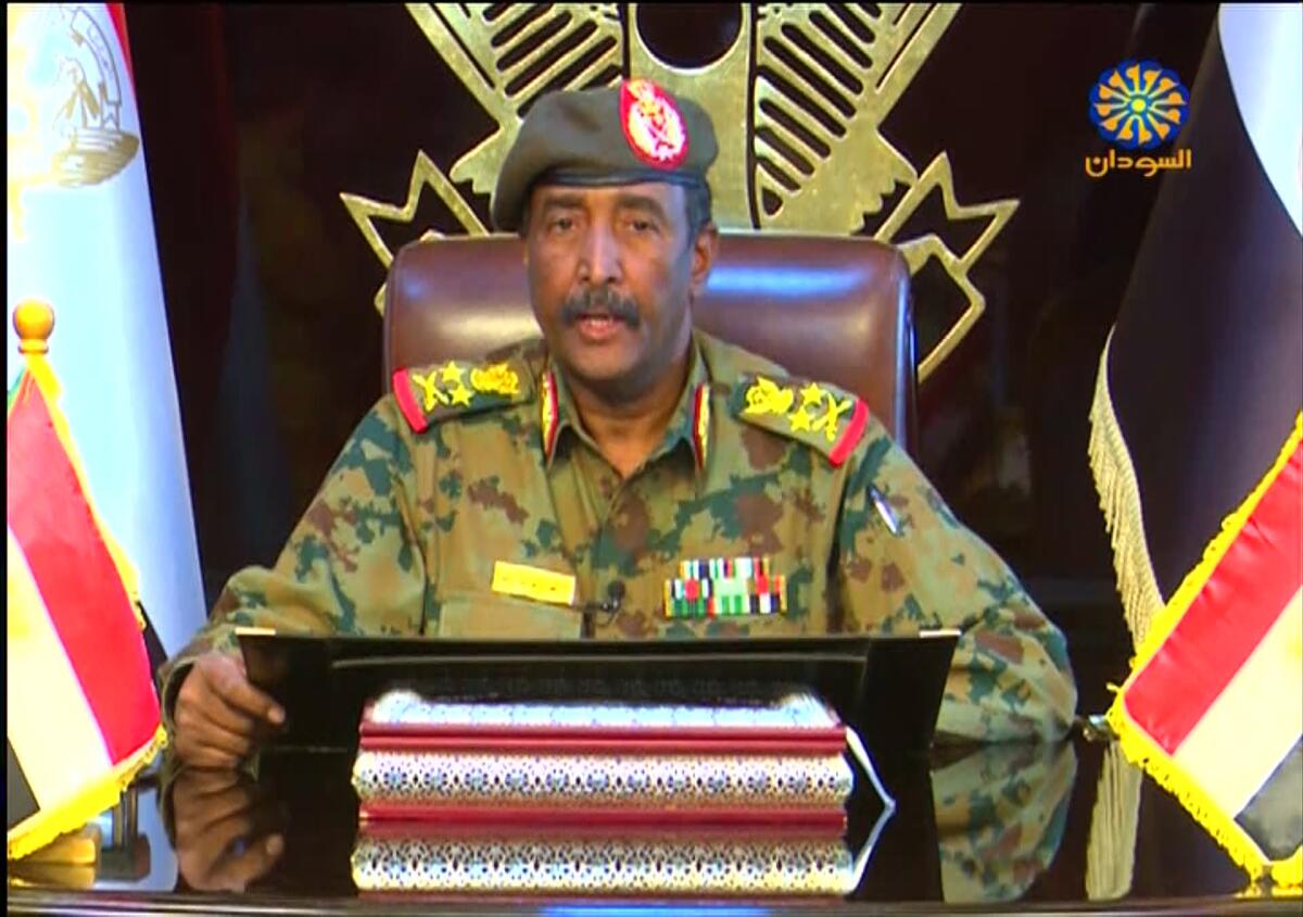Gen. Abdel-Fattah Burhan, head of Sudan’s ruling sovereign council, sits at a desk while flanked by two flags.