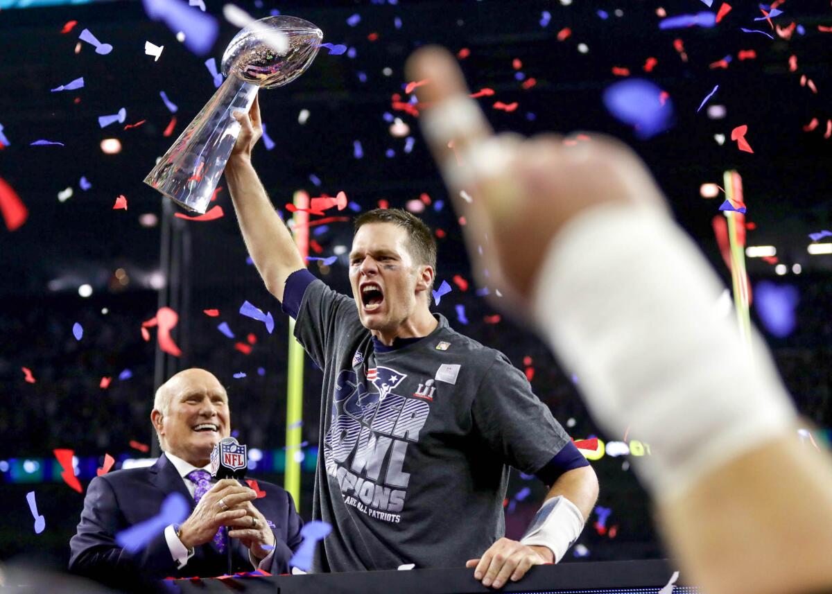 Tom Brady holds the Lombardi Trophy over his head, as broadcaster Terry Bradshaw watches, after a Super Bowl win.