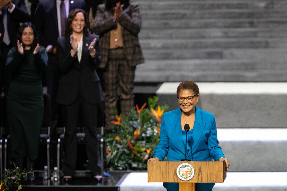 Mayor Karen Bass at a lectern, with Vice President Kamala Harris in the background