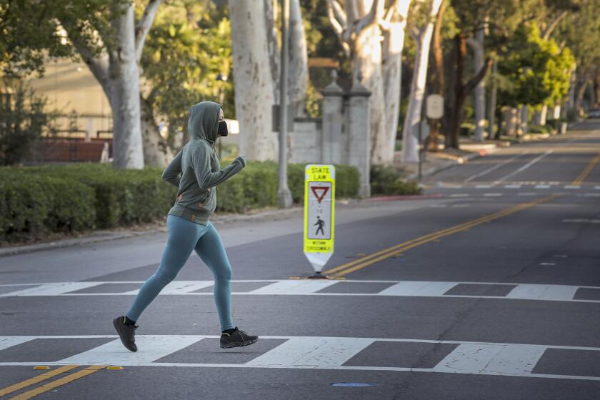 CLAREMONT, CA - MARCH 28, 2020 - A jogger in face mask crosses a street in Pomona College on the morning of Friday March 27, 2020 in Claremont. A student of the college was diagnosed for COVID-19 on Tuesday and informed the school Wednesday, Pomona College announced Thursday night. The student, whose name was not released, left campus March 13 and has not returned, according to a statement from the college. (Irfan Khan / Los Angeles Times)