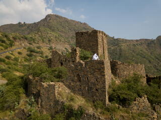 A person in white sits atop a structure that is part of a brick fort in a mountainous setting