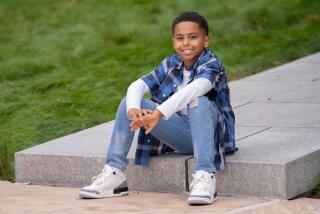 Ghalee Wadood Jr. sits outdoors on a concrete step at the end of a sidewalk, surrounded by grass.
