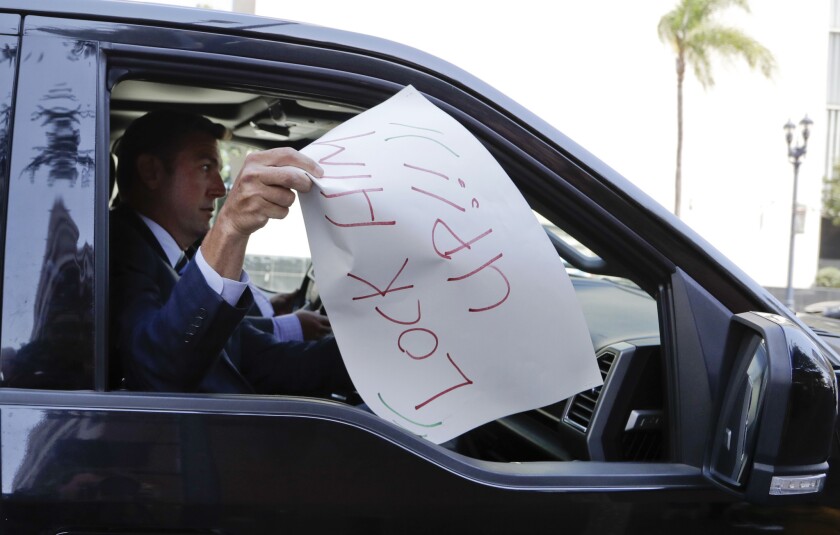 U.S. Rep. Duncan Hunter removes a sign that reads "lock him up," placed on the windshield of his car by a protester, as he leaves an arraignment Aug. 23, 2018, in San Diego.