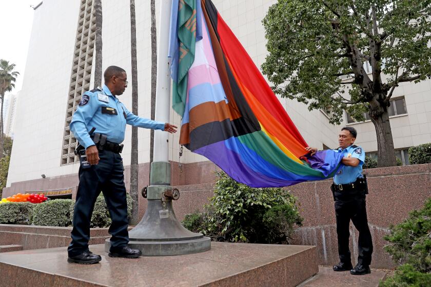 LOS ANGELES, CA - JUNE 01: Gregory Winfrey, left, and Benedicto Barnachea, security guards with Allied Universal, prepare to raise the Progress Pride Flag over the Kenneth Hahn Hall of Administration in downtown on Thursday, June 1, 2023 in Los Angeles, CA. L.A. County Supervisors Janice Hahn, Hilda Solis and Lindsey Horvath will join county Assessor Jeff Prang, and Sister Tootie Toot of the group the L.A. Sisters of Perpetual Indulgence to raise the Progress Pride Flag over the Kenneth Hahn Hall of Administration. It will mark the first time a pride flag has flown over a county building. (Gary Coronado / Los Angeles Times)