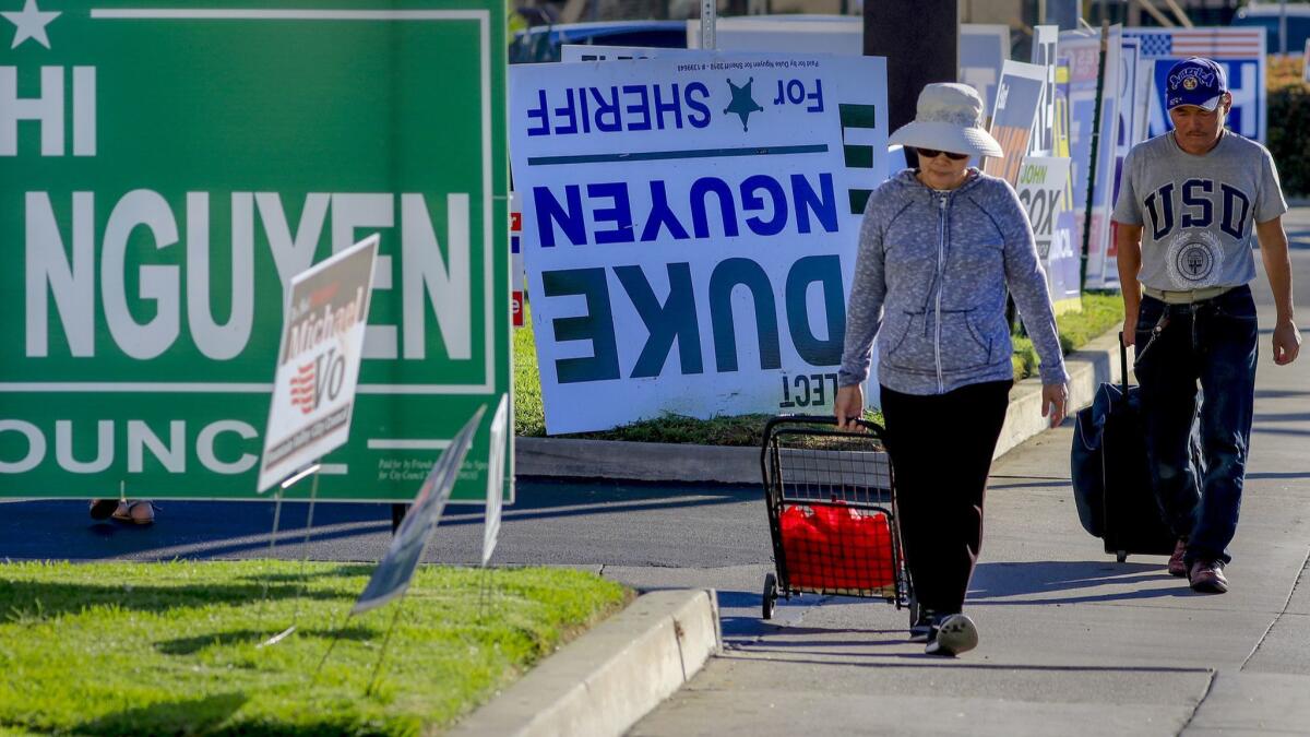 Pedestrians walk past a row of political signs and posters along Bolsa Avenue in Westminster. In Orange County, 24 people of Vietnamese descent are running for public office.