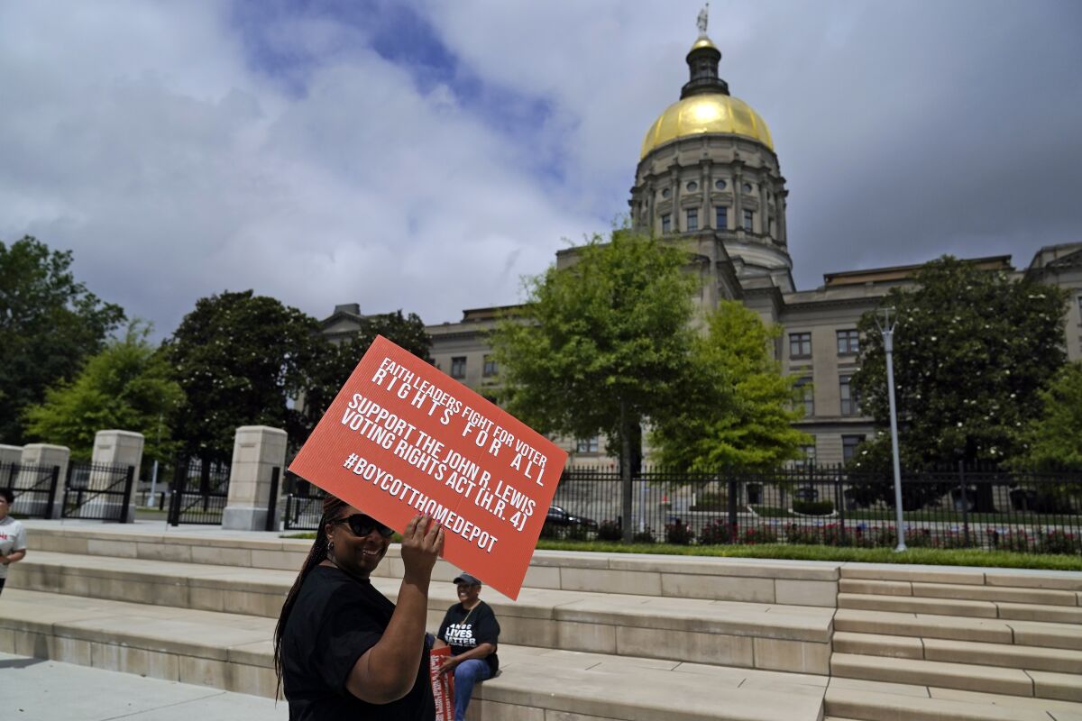 A Black man holds an orange sign in support of H.R. 4 in front of Liberty Plaza near the Georgia State Capitol.