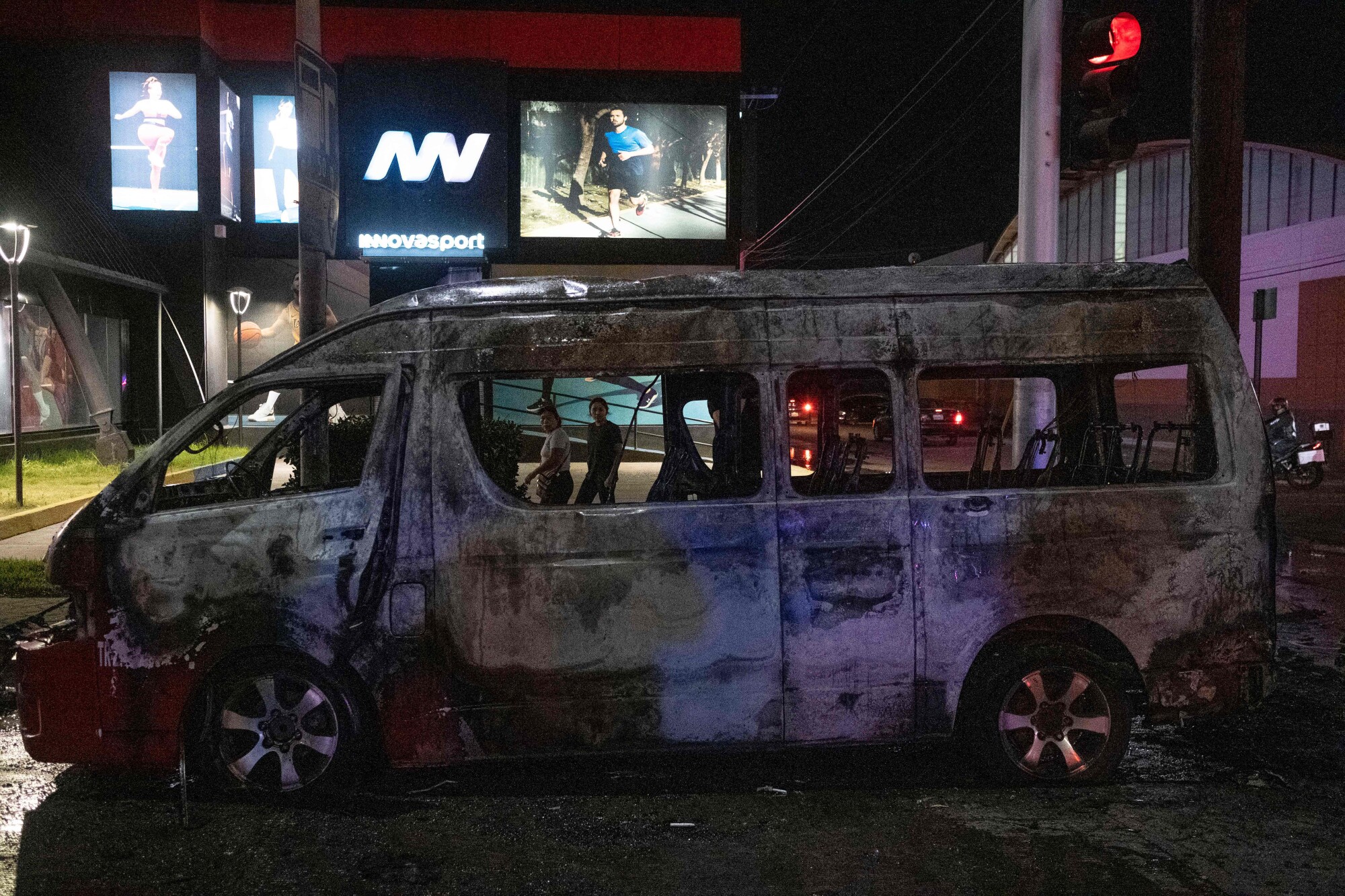 People look at a charred public transport vehicle after it was set on fire in Tijuana