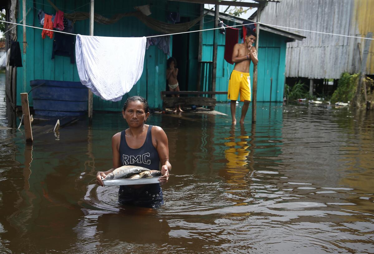 Edileuza Pereira da Silva lleva un plato con pescado para cocinar fuera de su casa, inundada por la crecida 