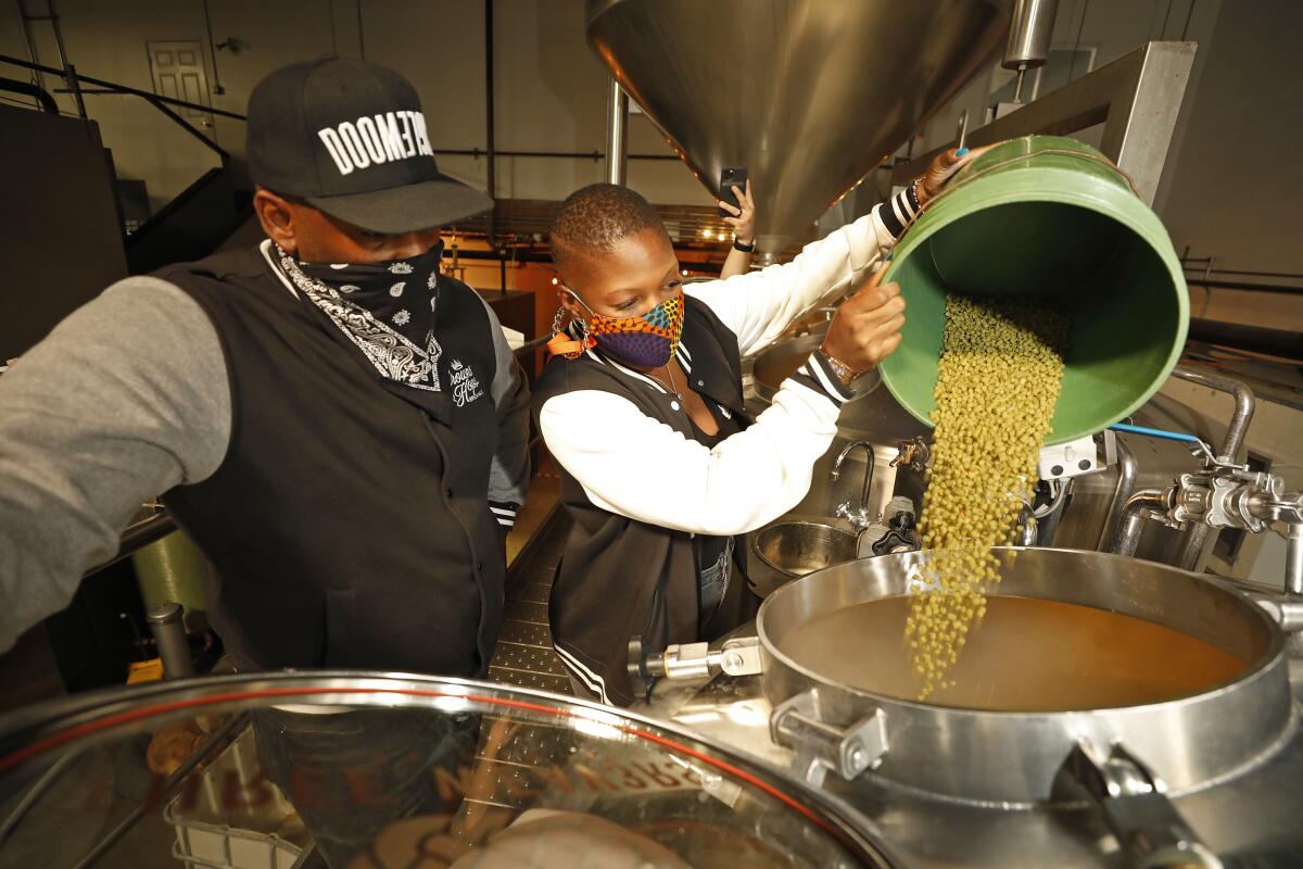 Two people pour hops into a brewing vat.