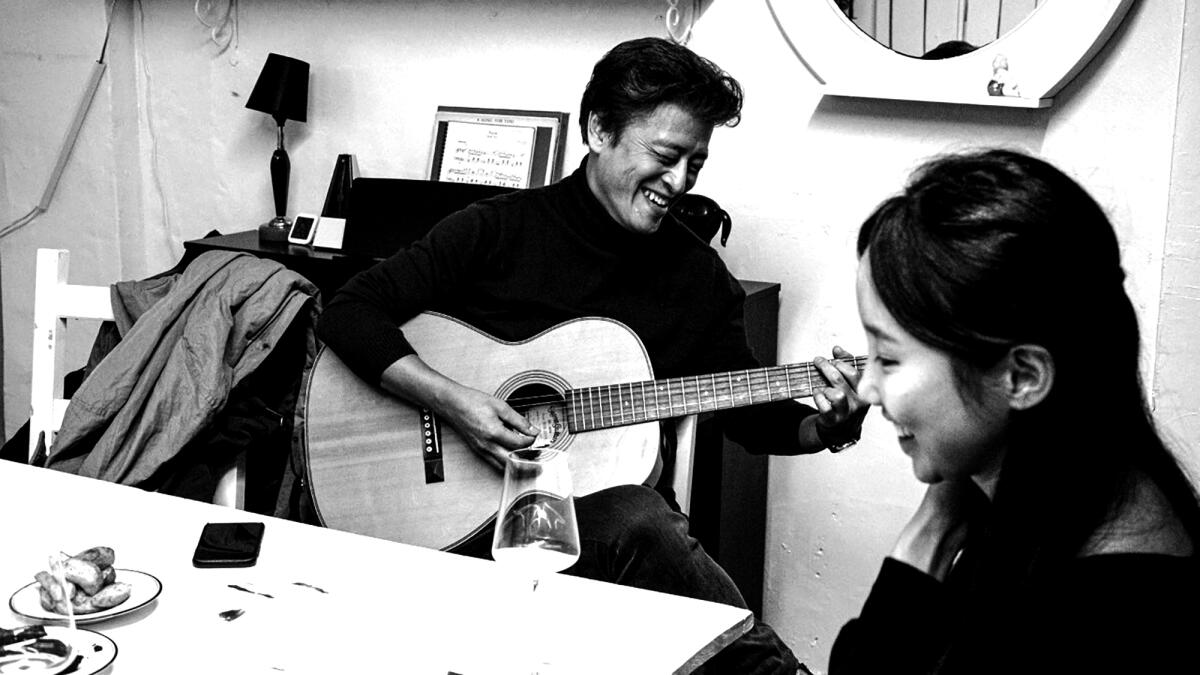 A man plays guitar while a woman smiles.