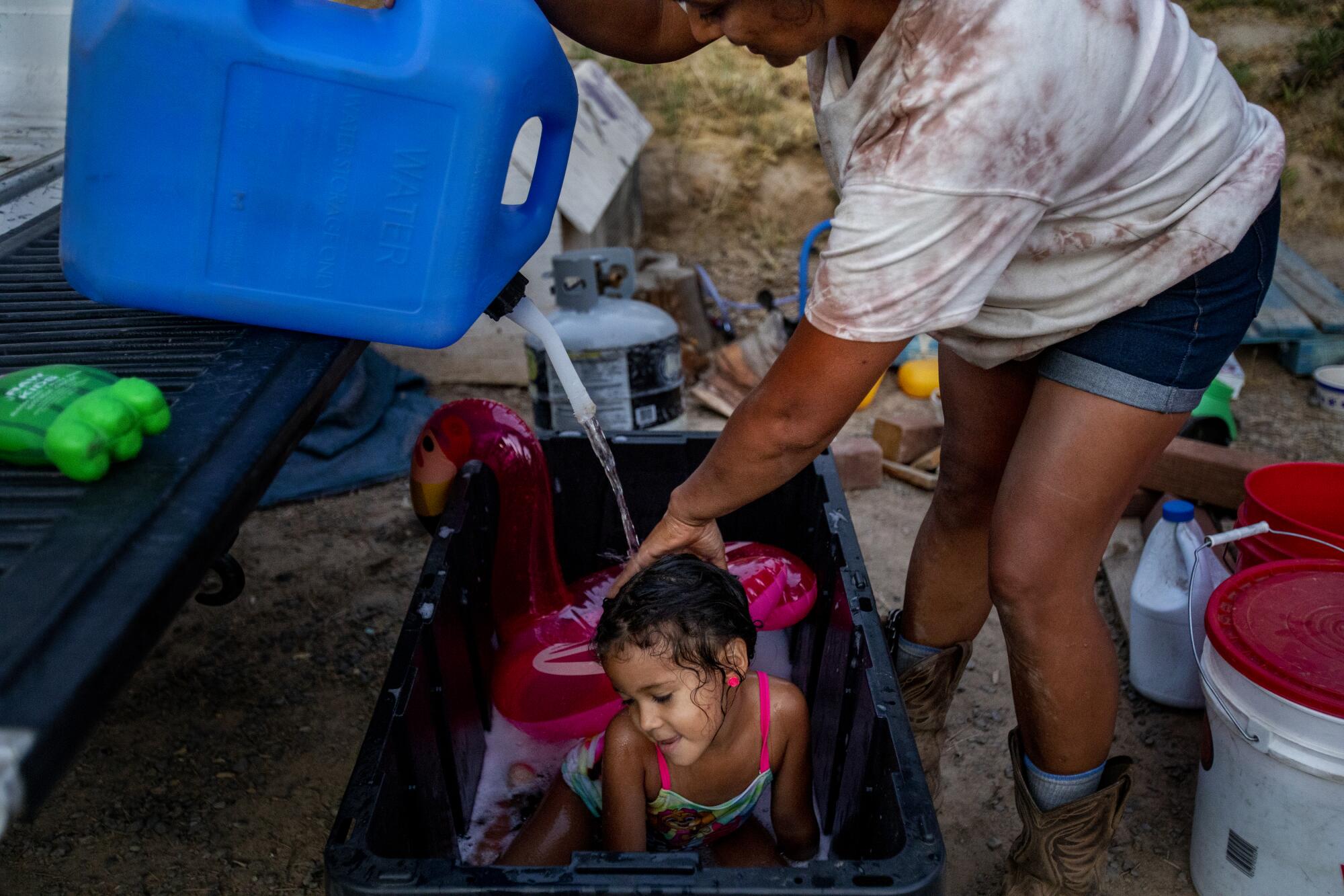 A woman bathes a young girl in a plastic bin