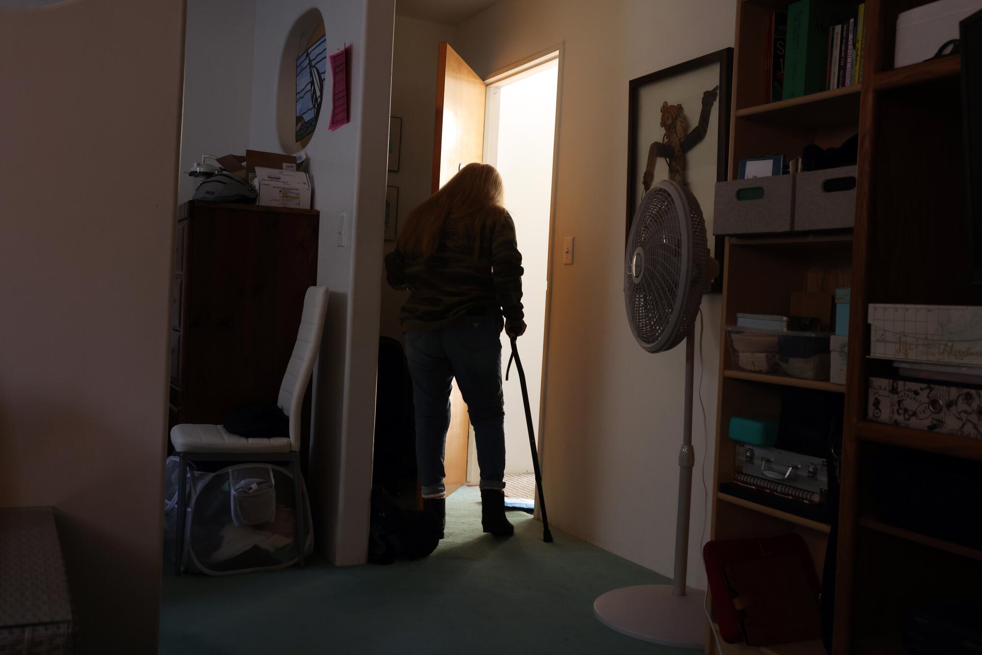 A woman walks to a door using a cane