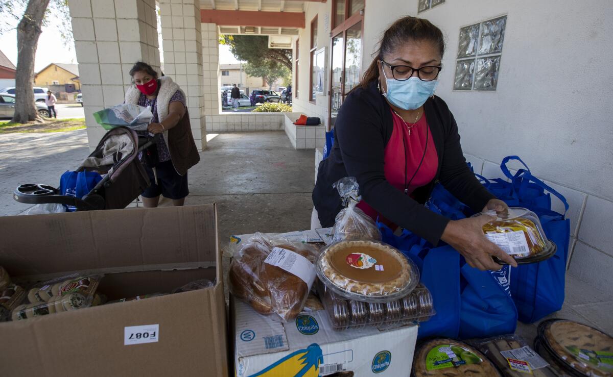 A woman in a mask takes food out of a bag and sets it on a table.