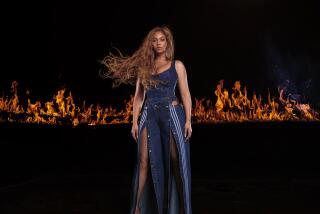 A woman with braided hair modeling a denim bodysuit and tracksuit, backed by flames