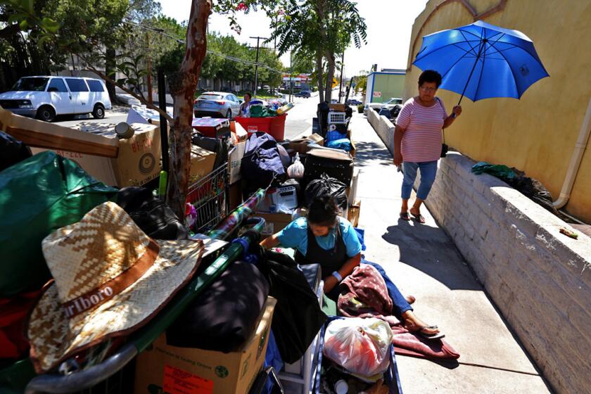 A pedestrian walks past Cecilia Hernandez, left, who rests with her belongings after private security kicked her out of the Sylmar Shopping Center, where she and her husband were living.