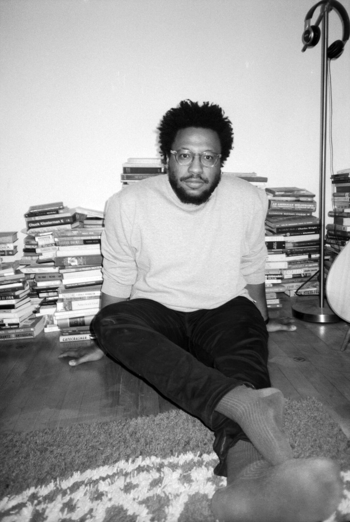 Writer Vinson Cunningham sits on the floor surrounded by books in Brooklyn.