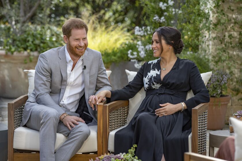 Prince Harry holds wife Meghan's hand as the two sit outdoors