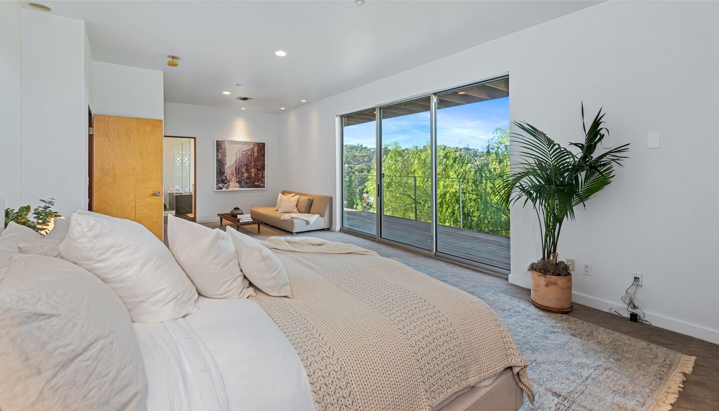 The bedroom is furnished and has glass walls overlooking trees and sky.