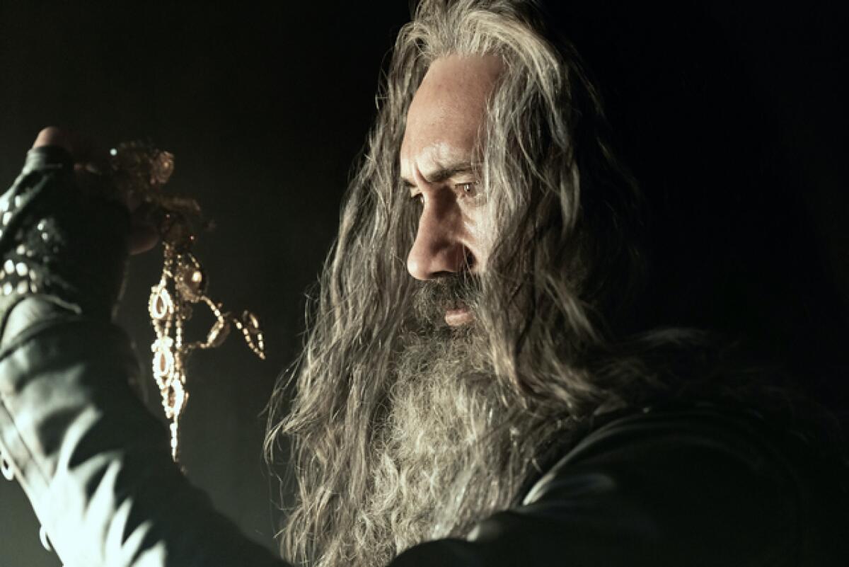 A man with a very long grey beard examines a piece of jewelry.
