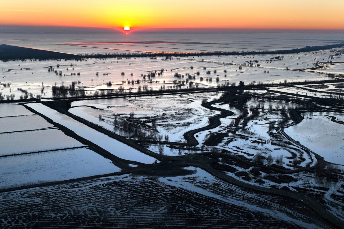 The sun rises over an agricultural landscape of flooded fields and mudflats separated by earthen banks.