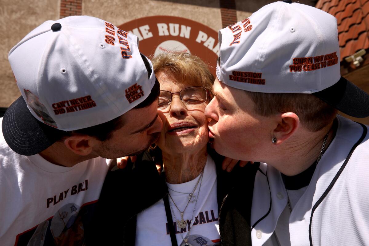 Two men in baseball caps kiss their grandmother at a memorial service.