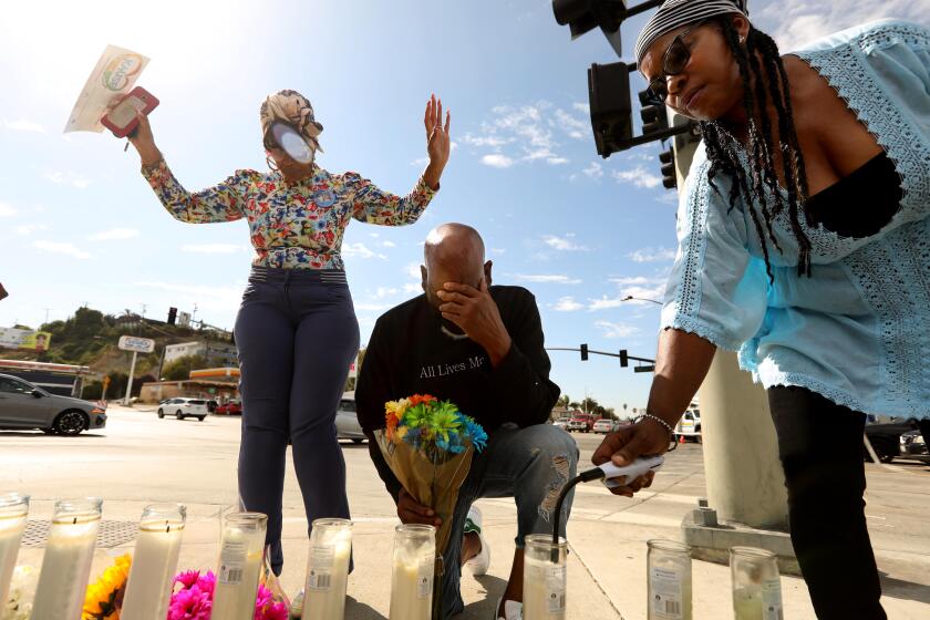 LOS ANGELES, CA - AUGUST 5, 2022 - - Carmen Dorsey, from left, and London Carter pray as Vera Jones lights a candle at a makeshift memorial across the street from where a fiery multi-car crash left six dead, including a pregnant woman, and injured others in Windsor Hills in Los Angeles on August 5, 2022. The accident happened on Thursday, August 4, 2022. (Genaro Molina / Los Angeles Times)