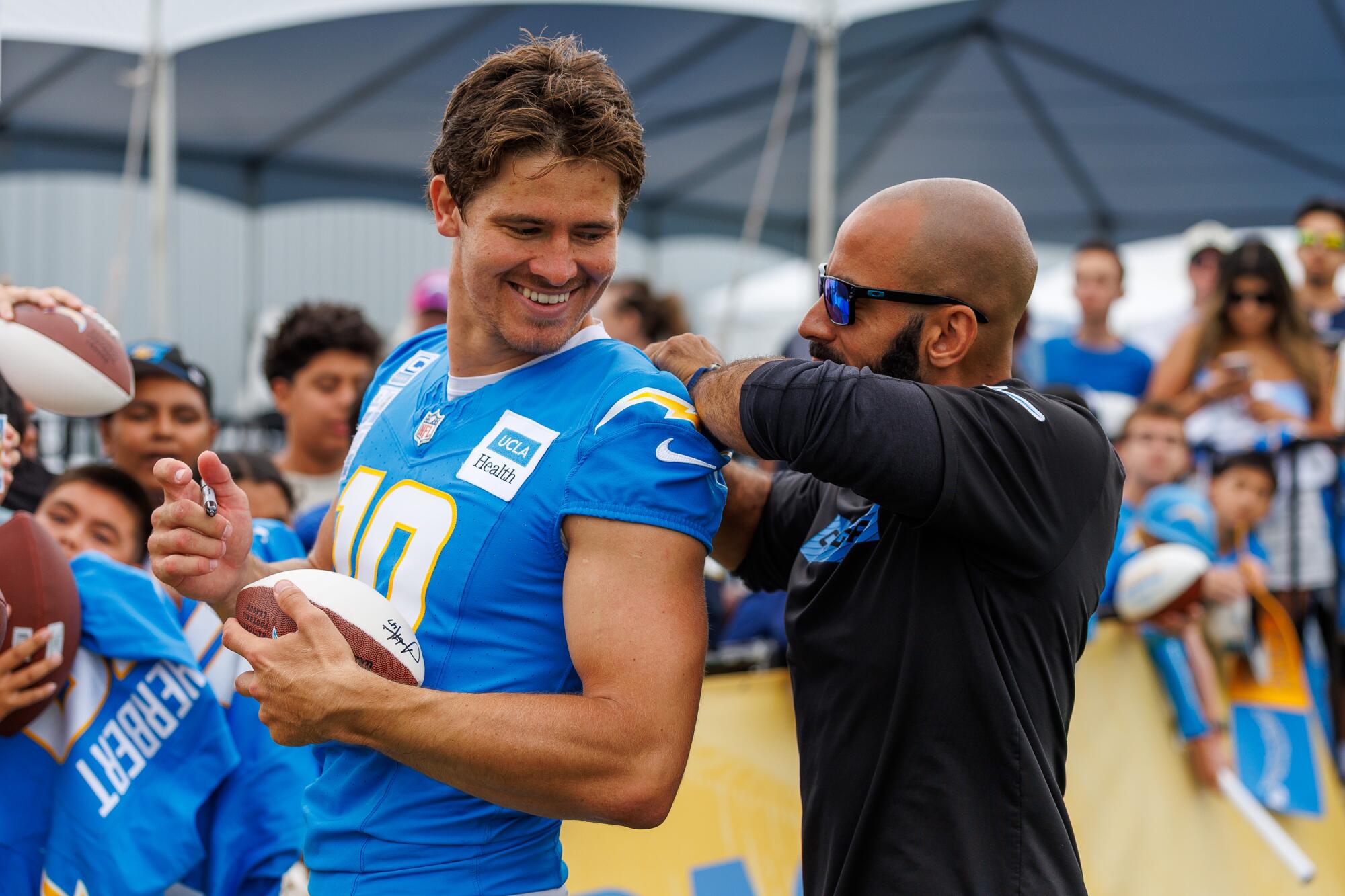 Chargers strength and conditioning coach Devin Woodhouse helps quarterback Justin Herbert with his jersey.