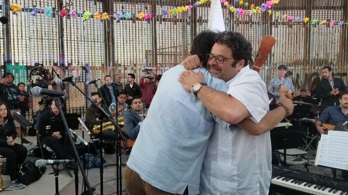Arturo O'Farrill (right) and Jorge Castillo hug after performing at a May 2018 concert on the Tijuana side of the U.S.-Mexico border that was led by four-time Grammy Award winner O'Farrill. That concert, and another held simultaneously on both sides of the border, has resulted in a documentary film, a book and a two-CD album that will be the basis for the March 14 "Fandango at the Wall" concert at San Diego's Copley Symphony Hall.