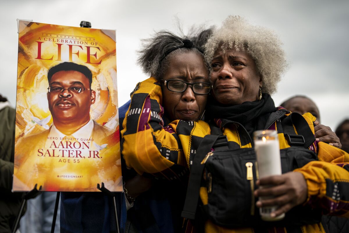Two crying women hug; one holds a votive candle. Next to them a sign says "Celebration of Life" and "Aaron Salter Jr."