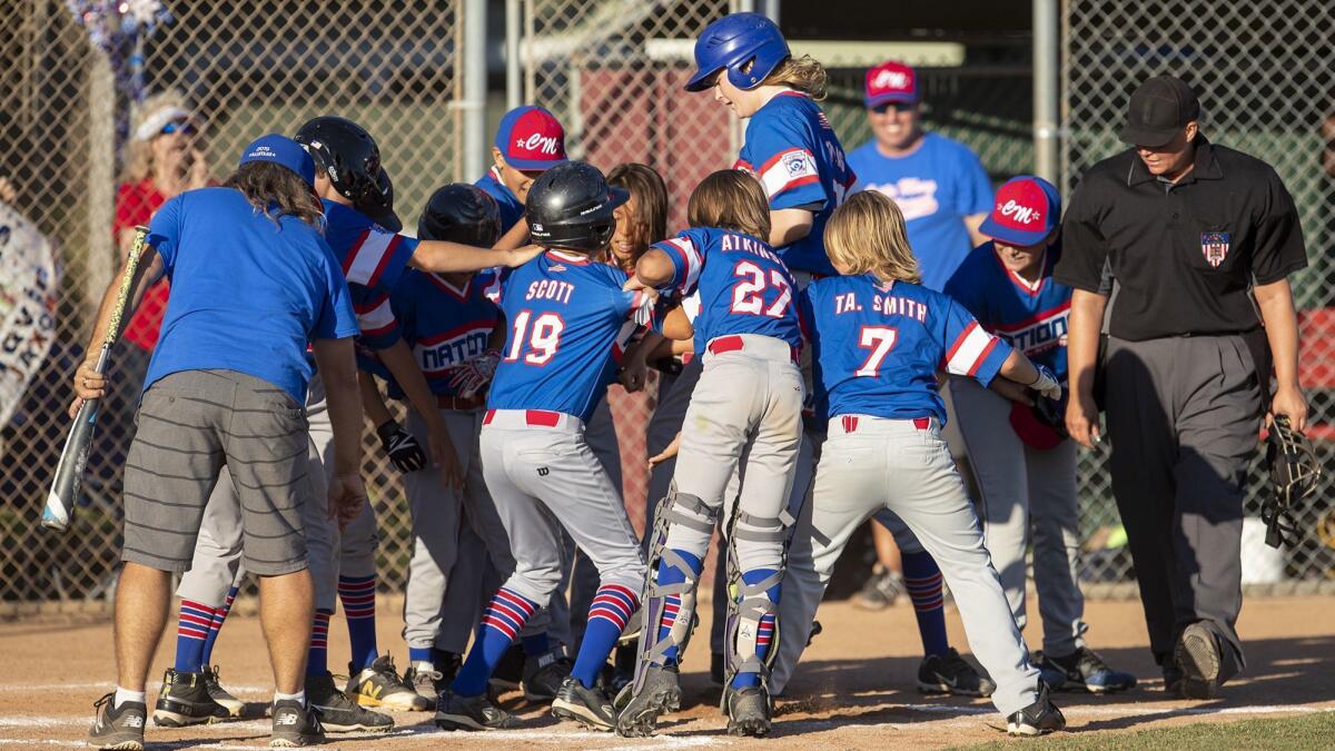 Costa Mesa National Little League's Peyton Thomas, center, is mobbed by teammates at the plate after she hit a walk-off home run to beat Costa Mesa American Little League in the Mayor's Cup on July 11, 2019.