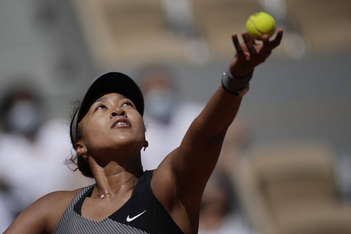 A woman in a visor lifting a tennis ball into the air.