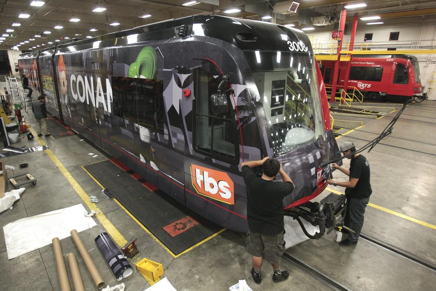 David Garcia, left, and Anthony Soltero wrap the front of a trolley car as they and a crew put on an advertising wrap for TBS television host Conan O'Brien's talk show on the trolley car.