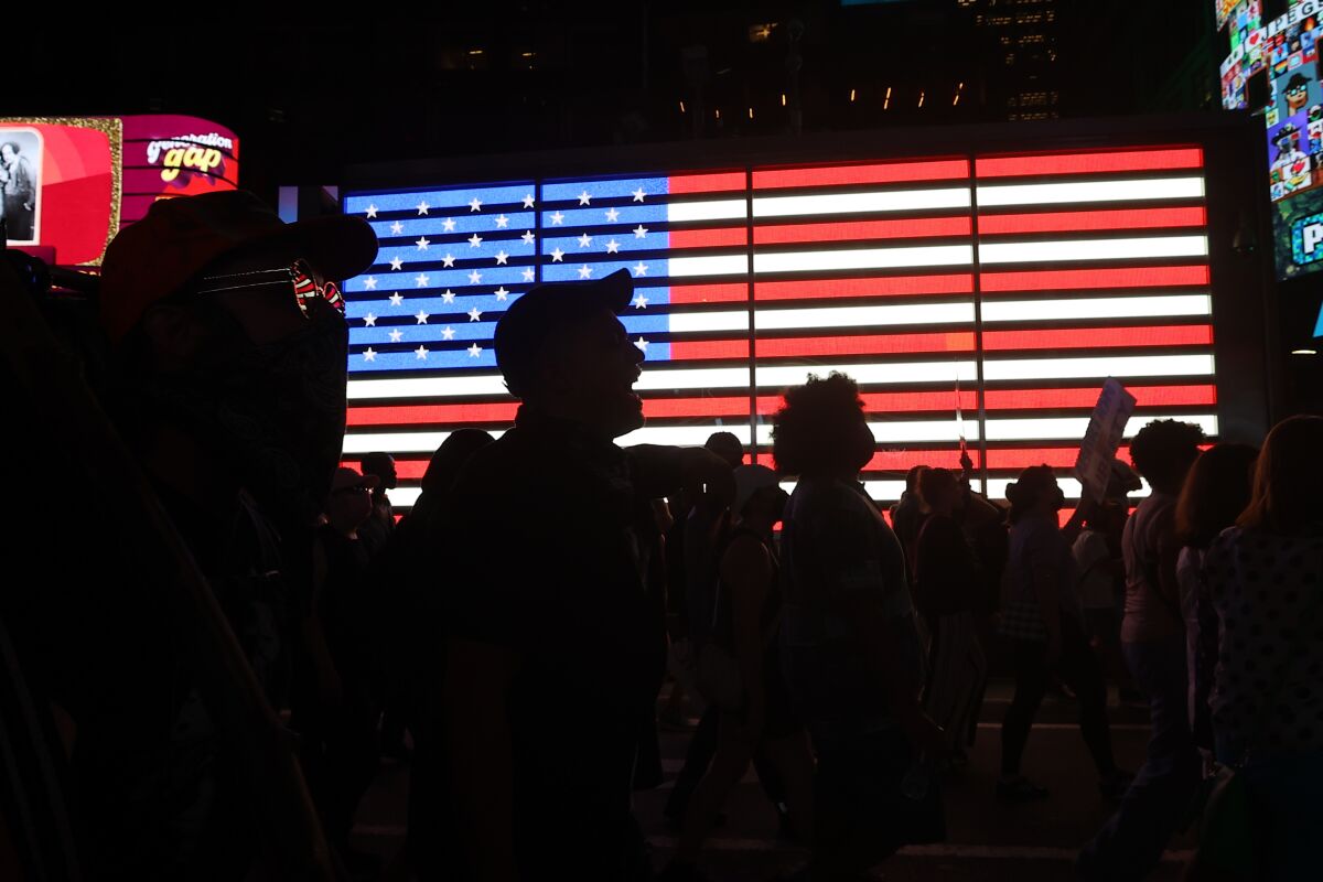 Silhouettes of people in a crowd are shown against a digital U.S. flag. 