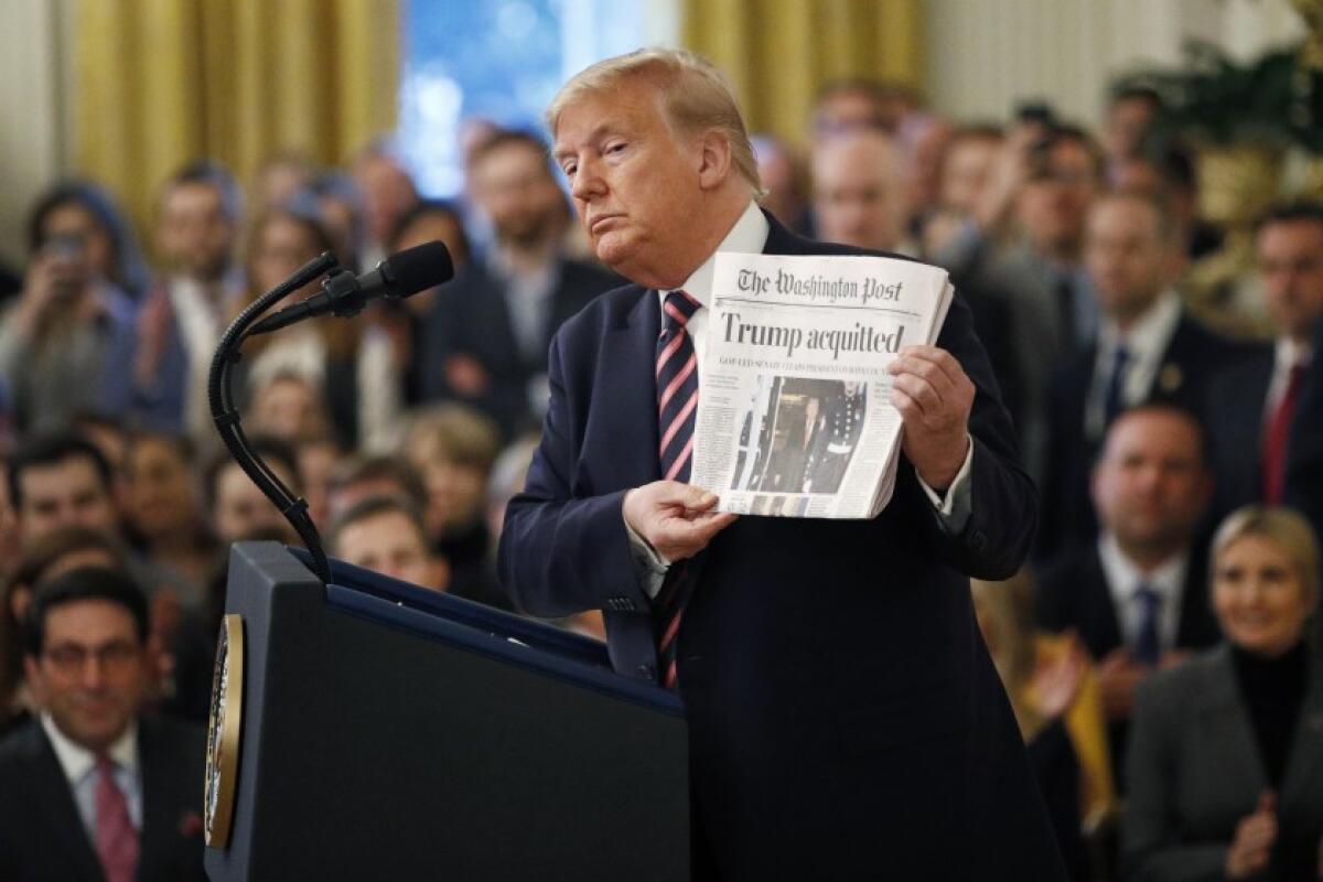 President Trump holds up a Washington Post with the headline "Trump acquitted" as he speaks in the East Room of the White House on Feb. 6.