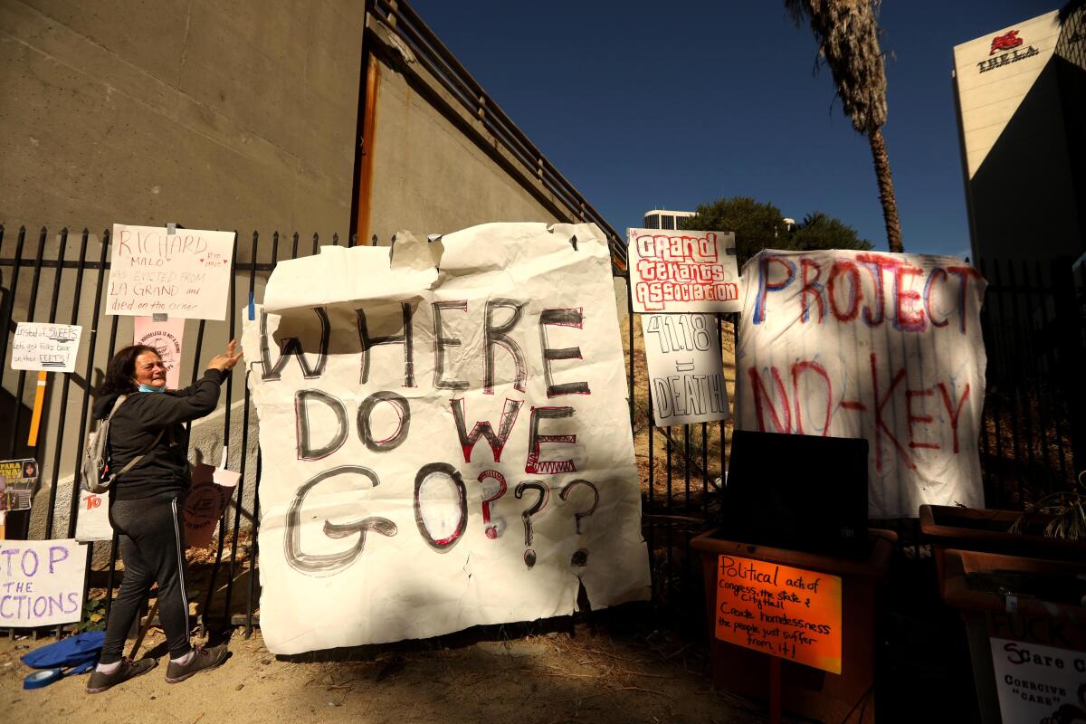 A woman stands next to protest signs on a gate