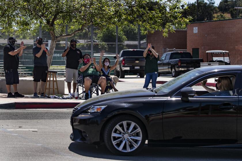 RIVERSIDE, CALIFORNIA - MAY 5, 2020: Faculty and staff members cheer as seniors drive by after picking up their caps and gowns at Poly High School in the midst of the ongoing coronavirus pandemic on May 5, 2020 in Riverside, California. There won't be a graduation this year.(Gina Ferazzi/Los Angeles Times)