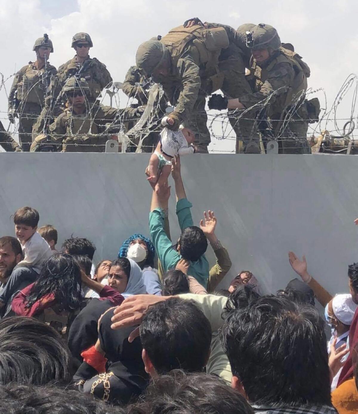 An infant is handed up from a crowd to a U.S. Marine