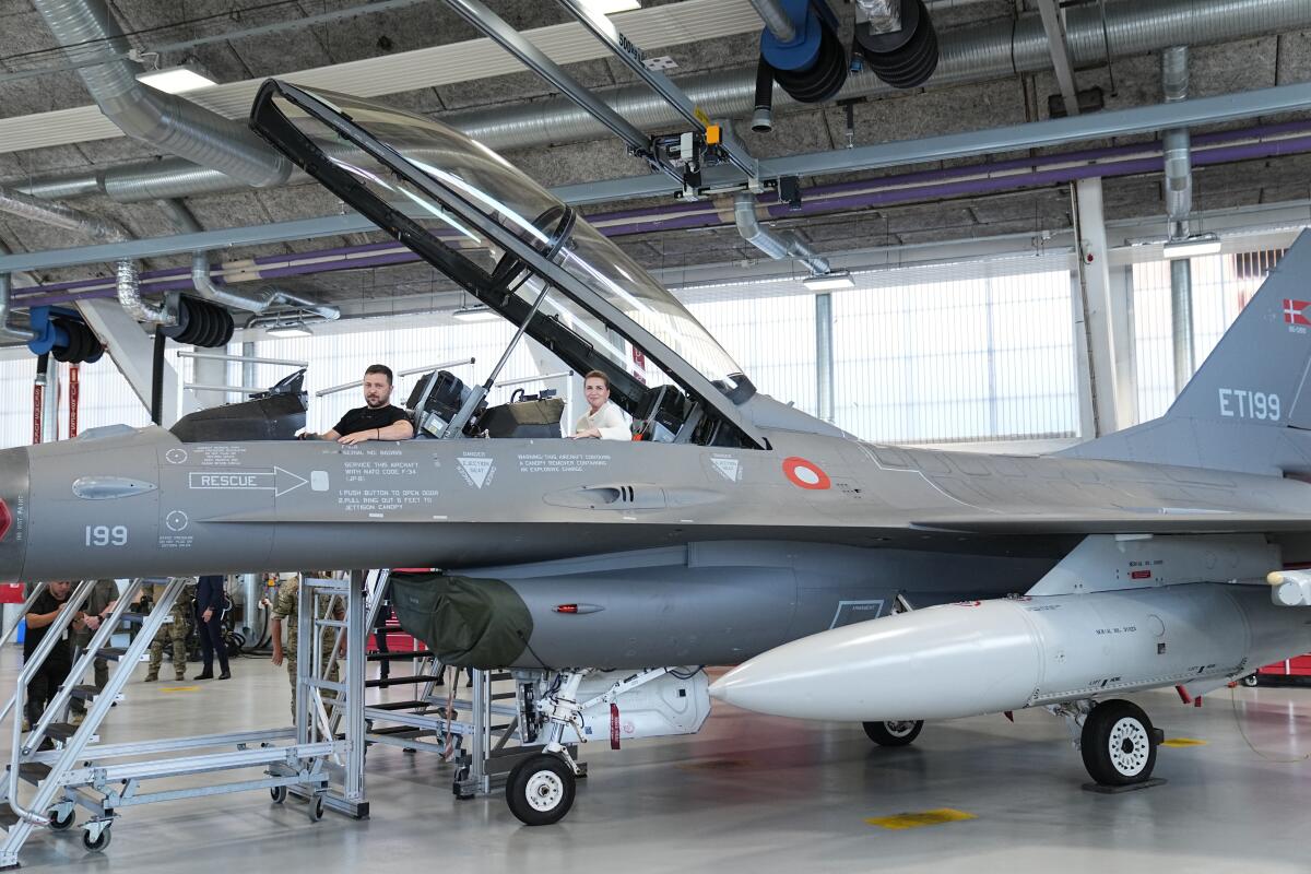 Two men sit in a parked F-16 fighter jet.