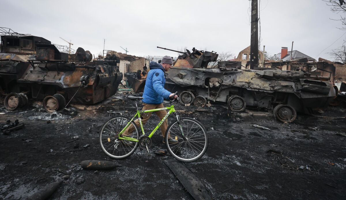 A man walks his bike past bomb damage and Russian military vehicles