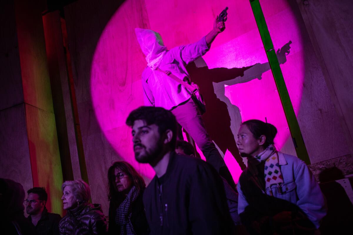 A performer appears from behind the kinetic walls around the audience in a train scene, with lighting design by Jeanette Oi-Suk Yew and scenic design by Carlo Maghirang in the opera, "Sweet Land."