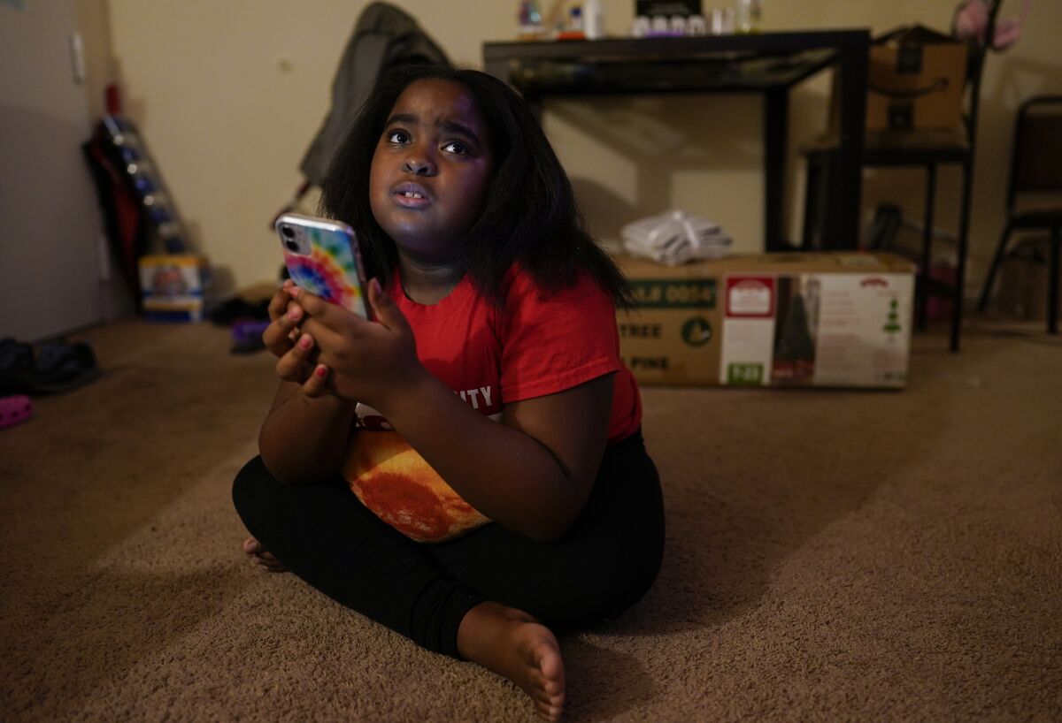 Brooklynn Chiles, 8, glances up from her smart phone at home inWashington, Sunday, Jan. 9, 2022. 