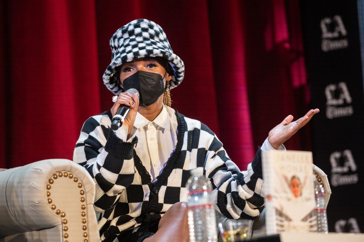 Janelle Monáe wears a black-and-white checkered outfit and speaks into a microphone.