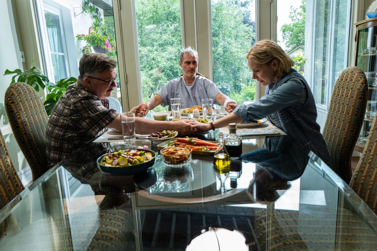 Nathan Lane, Joaquin Phoenix and Amy Ryan hold hands around a dinner table