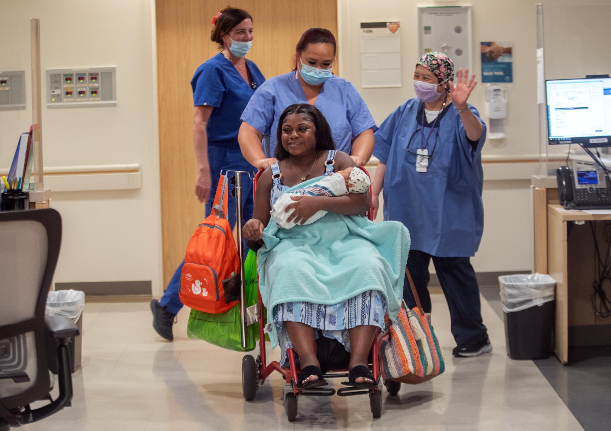 A woman holding her baby is wheeled through a hospital in a wheelchair.