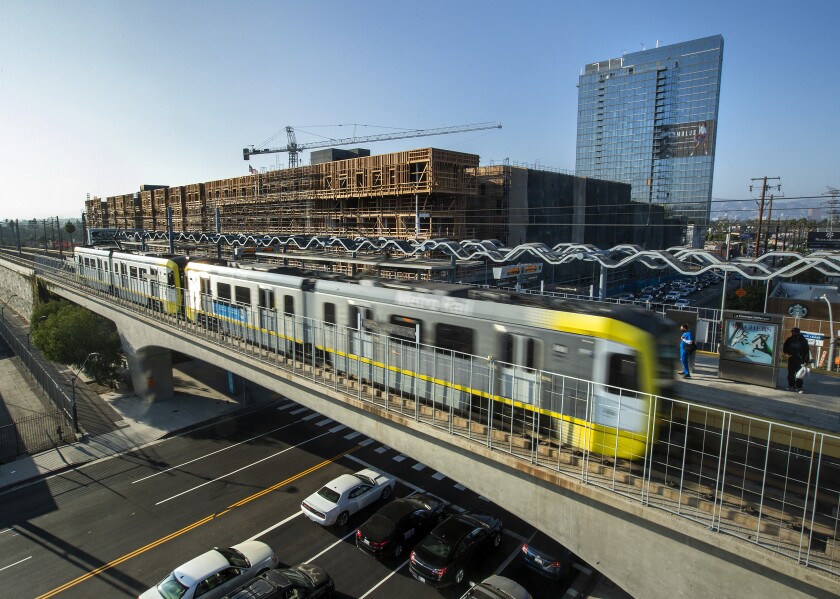 A train is seen moving across an overpass with cars beneath. In the background is a partially built structure.